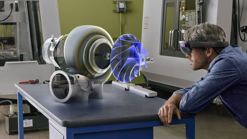「HoloLens」使用のイメージ写真 HoloLensを装着した男性が机の上の機械の構造を確認している